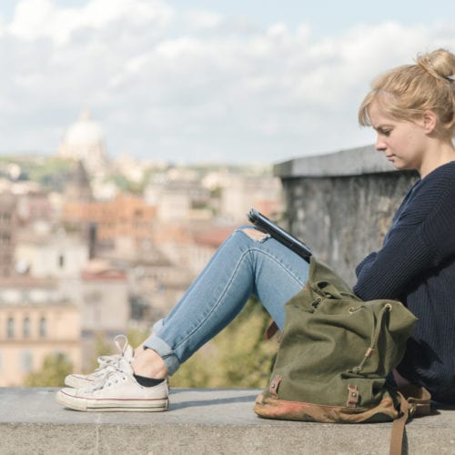 A young woman reading an electronic book outdoors in the park in Rome, Italy.